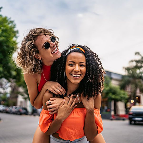 Two happy women piggy back riding down the street