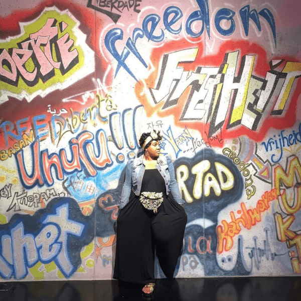 A graffiti artist in front of her wall of art