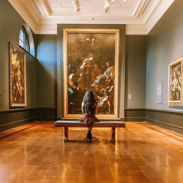 A woman sitting in an art museum looking at a painting