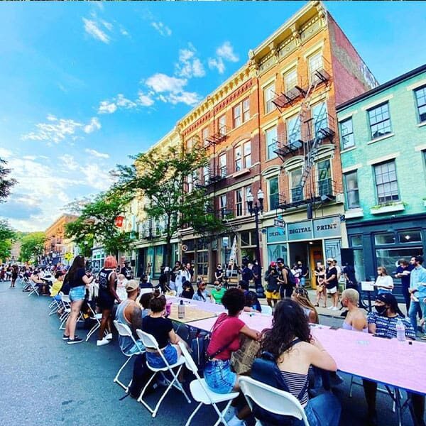 A long table of people sitting along a city street